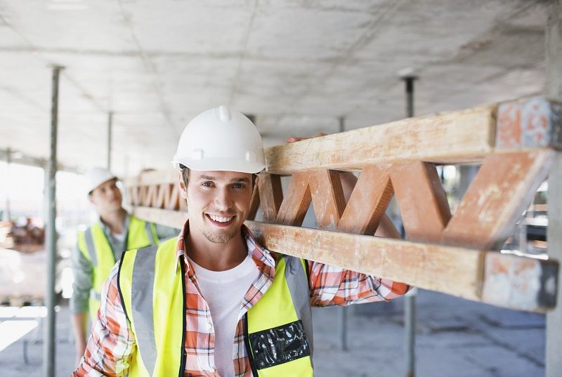Construction worker carrying girder on construction site comp
