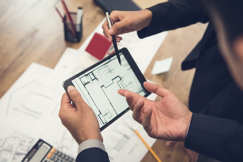 Real-estate-agent-with-client-or-architect-team-checking-a-housing-model-and-its-blueprints-digitally-using-a-tablet-cm