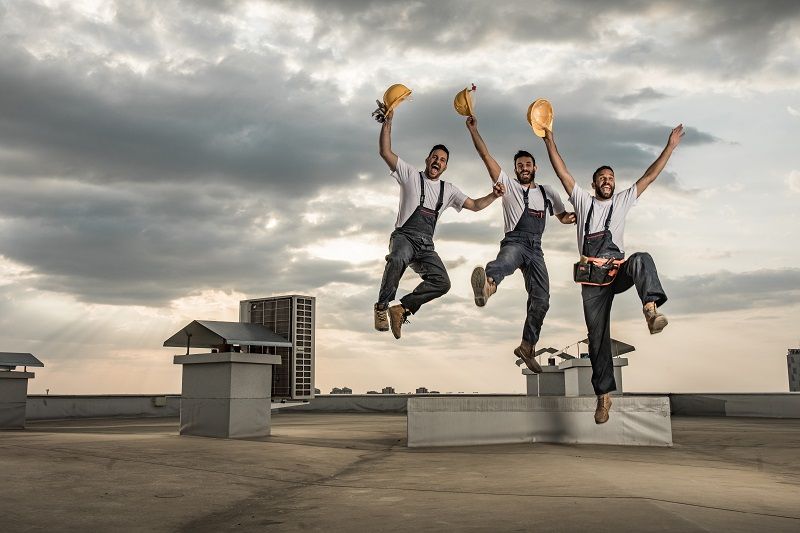 Team-of-playful-manual-workers-having-fun-while-jumping-on-a-roof.-cm