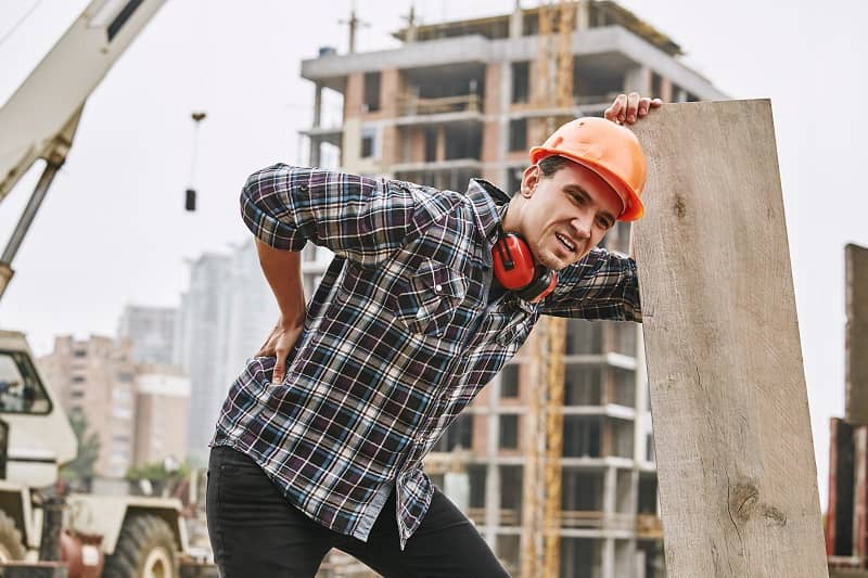Hard work. Construction worker in protective helmet feeling back pain while working at construction site. Building construction. Pain concept-cm