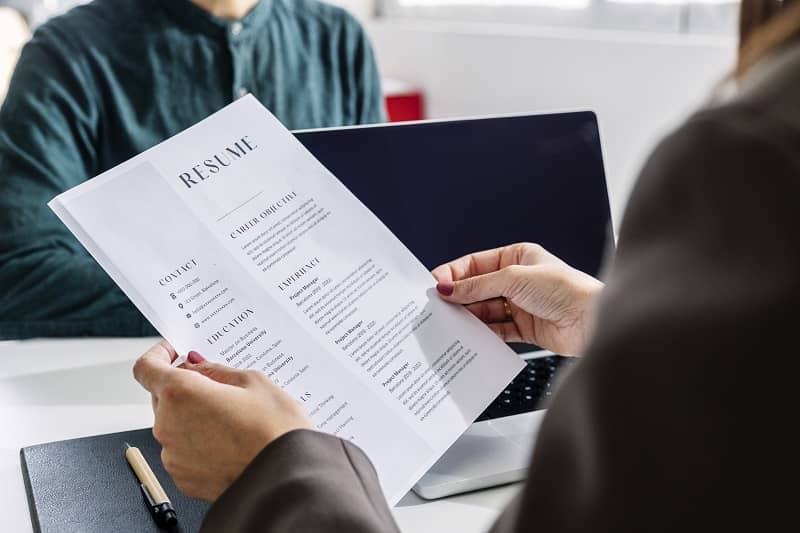 Hands of recruiter holding resume in front of candidate at desk-cm