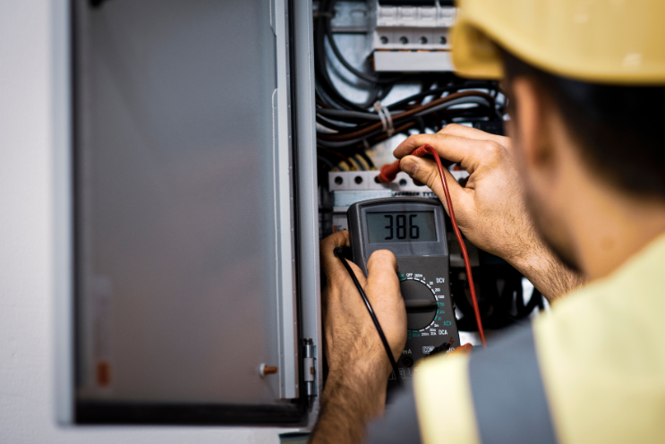 Electrician using a multimeter to measure voltage in an electrical panel — a highly in demand skilled trade.