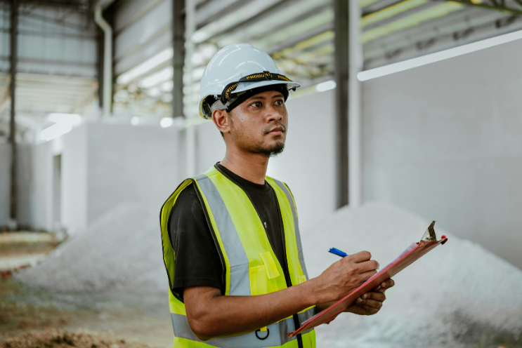 Construction worker in safety gear holding a clipboard on a jobsite, demonstrating responsibility and oversight