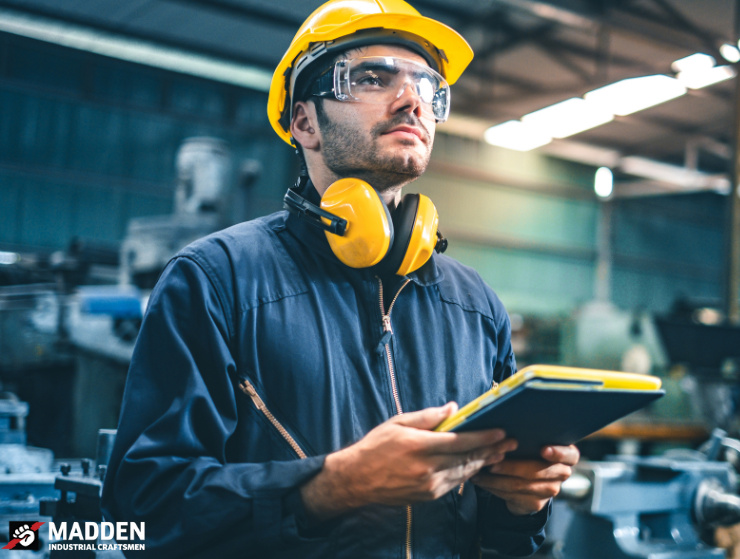Industrial worker with safety gear and clipboard in factory | Madden Industrial Craftsmen